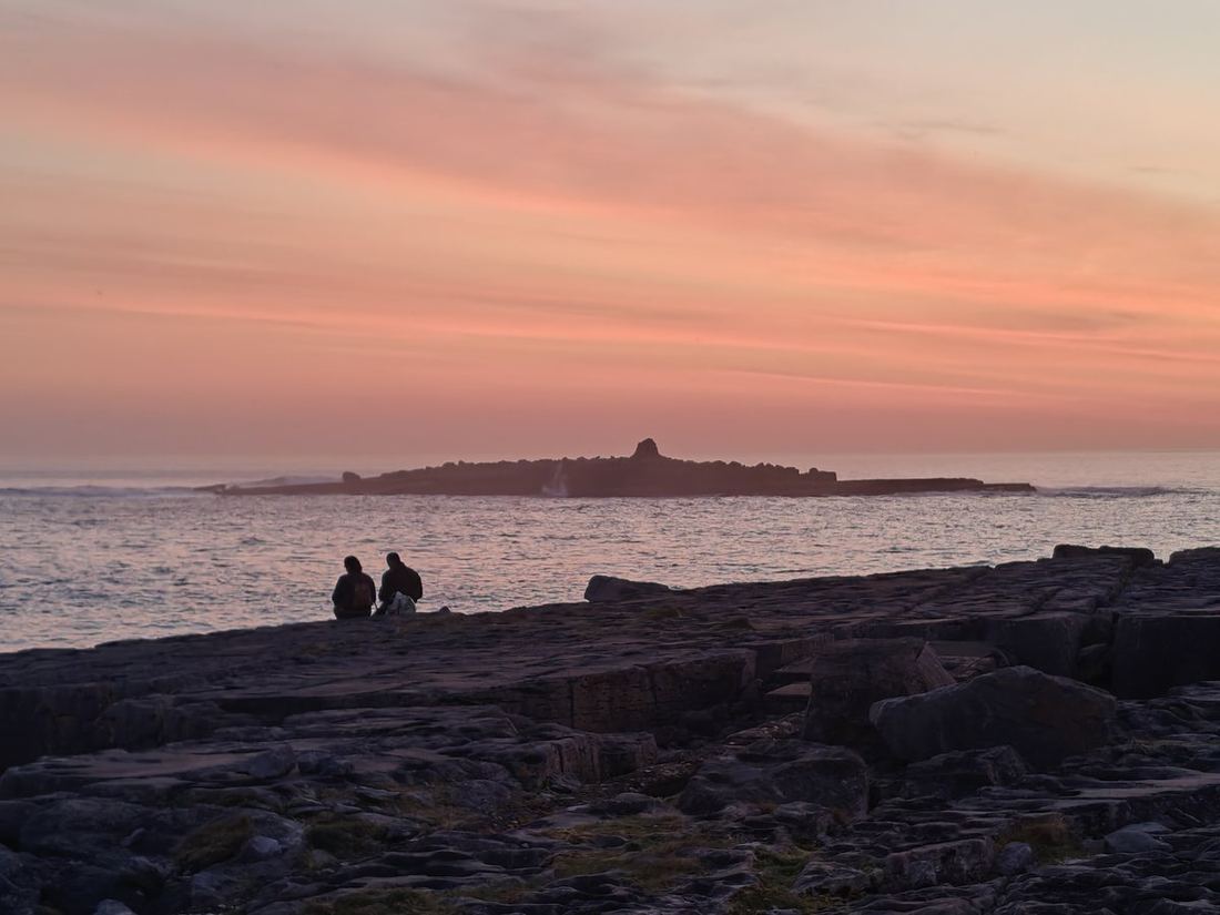 Two people watching the sun set over the sea from the rocks