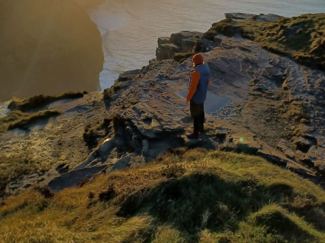 A walker on the cliff edge above the Atlantic in evening light